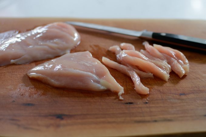 Chicken breast strips on a cutting board.