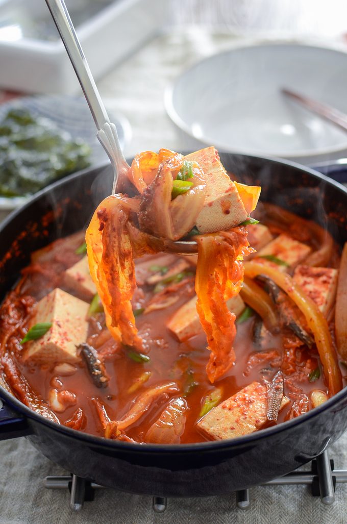 A ladle of anchovy kimchi stew and toful in a pot is ready to serve