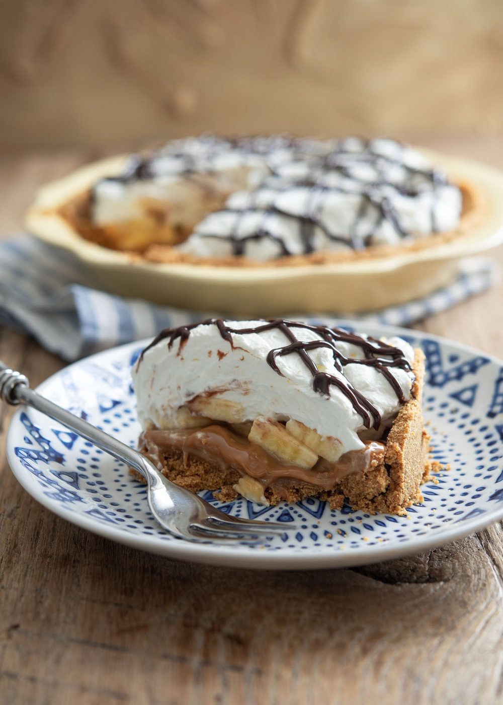 A slice of banoffee pie is served on a blue plate with a fork.