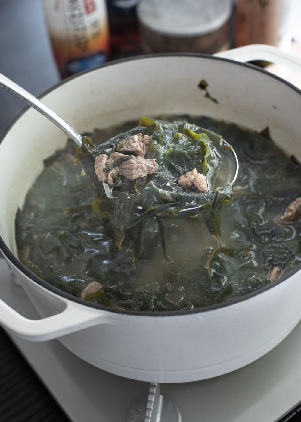 A ladle scooping Korean seaweed soup (miyeokguk) with beef from a pot.