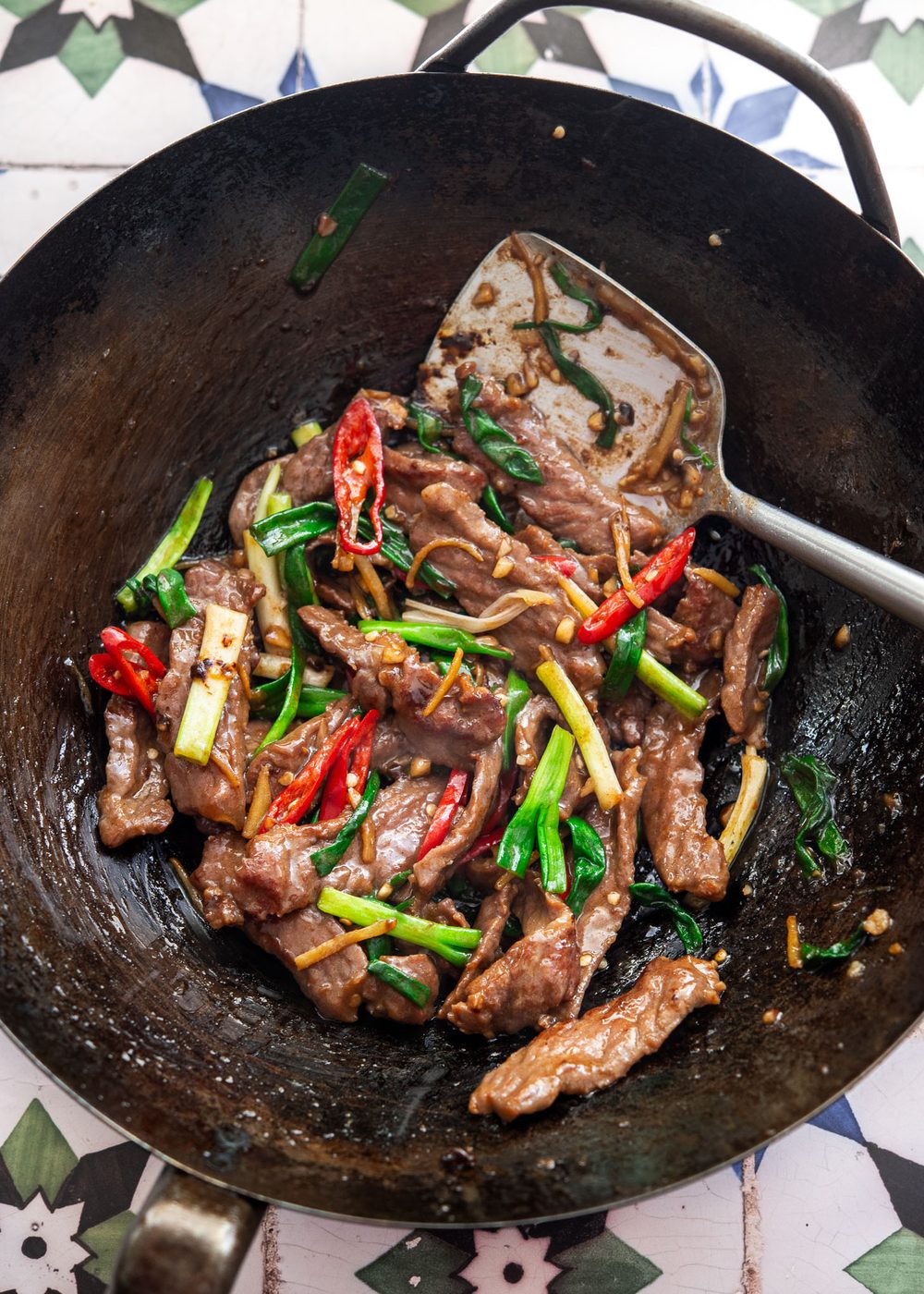 Ginger beef stir-fry with green onion and red chili cooked in a hot wok.