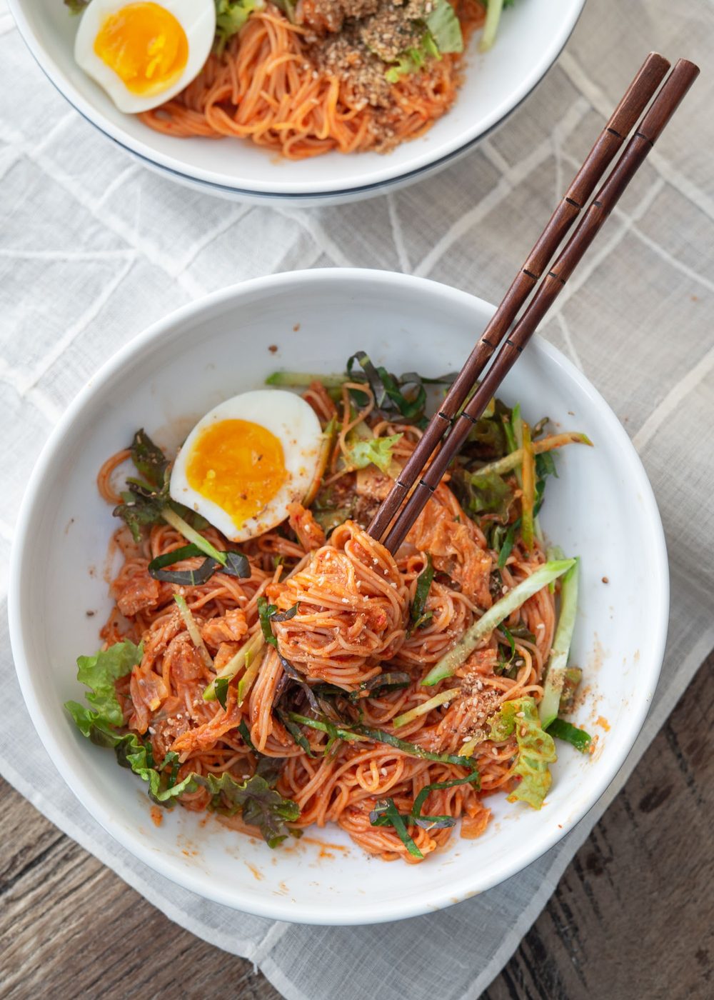 Chopsticks lifting bibim guksu noodles coated in spicy gochujang sauce from a bowl