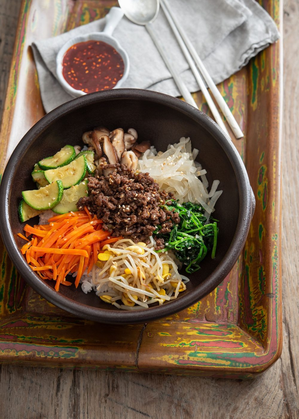 Mixed Korean rice bowl with ground beef, vegetables, and gochujang on a wooden tray