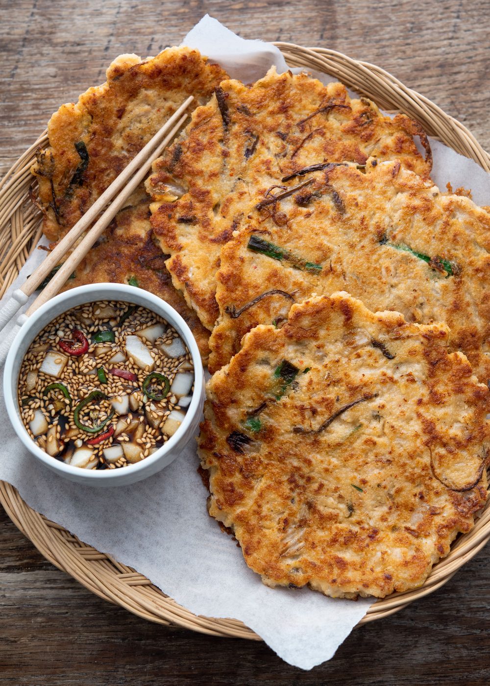 Crispy Korean bindaetteok arranged in a basket with soy dipping sauce and chopsticks