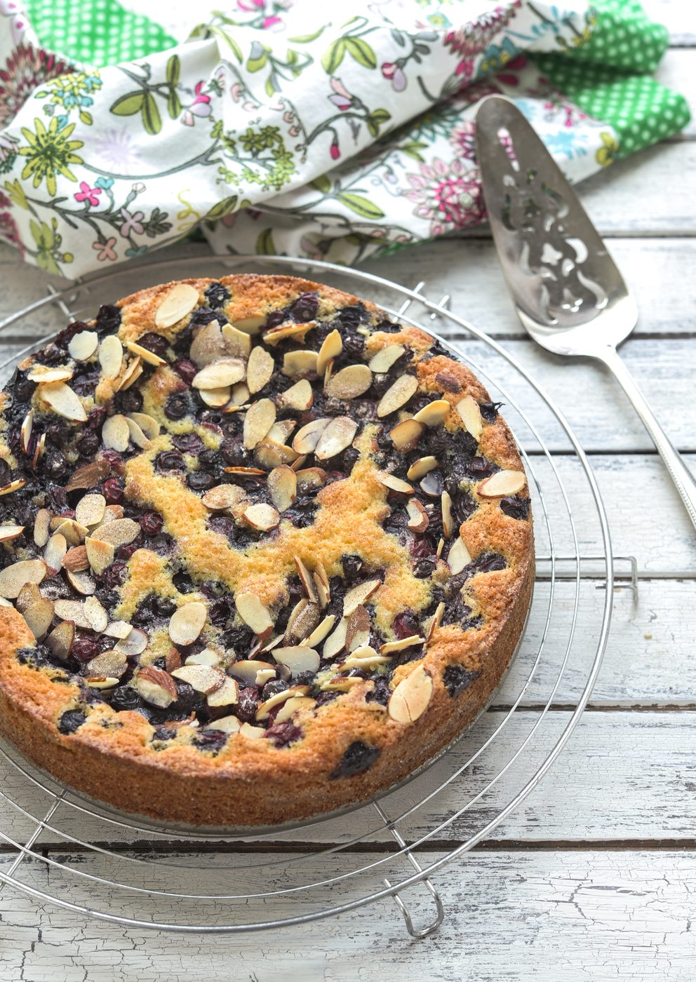 This direct blueberry cake topped with almond slices is cooling on a wired rack.