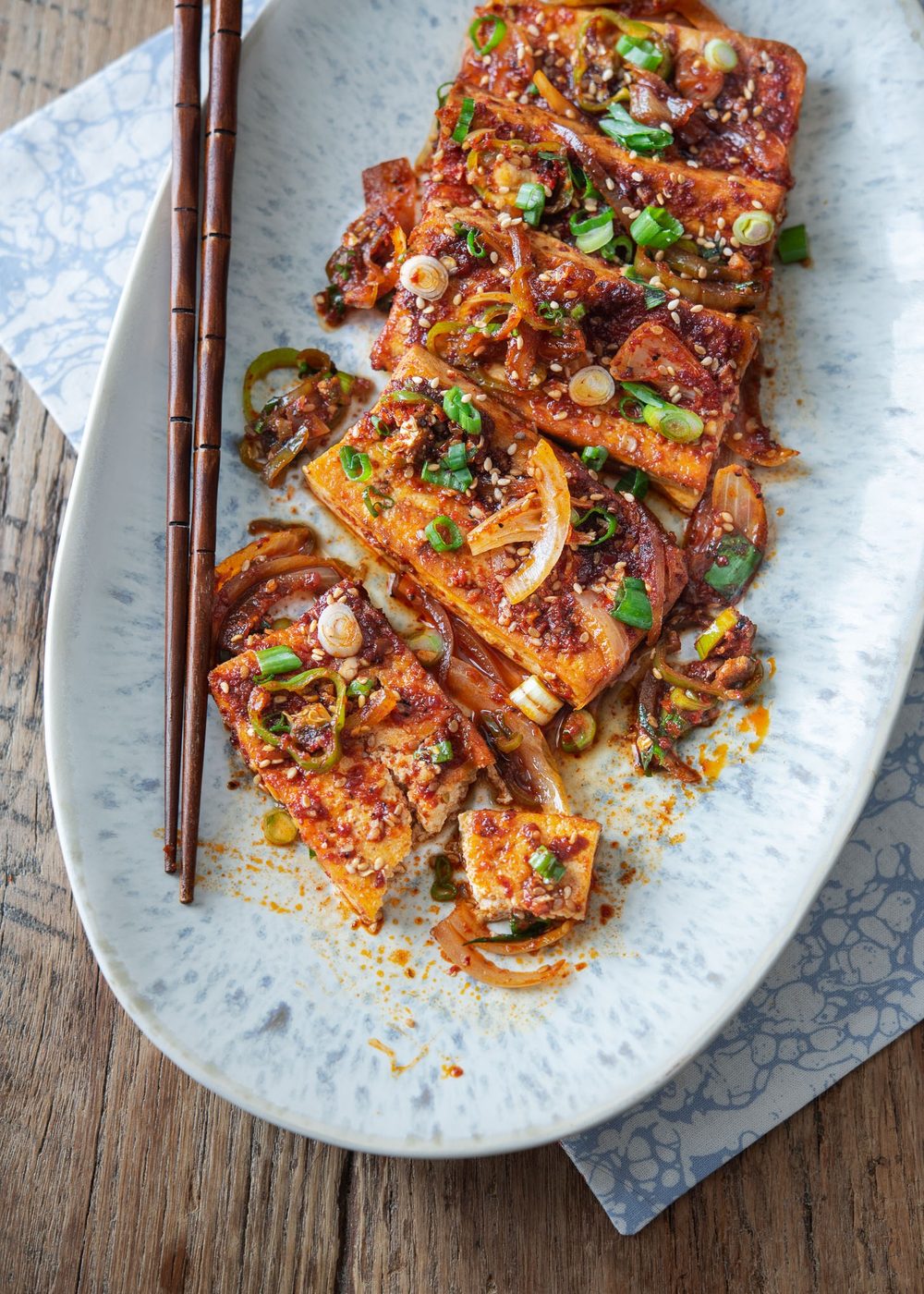 Spicy braised tofu slices are placed in an oval platter with a pair of chopsticks