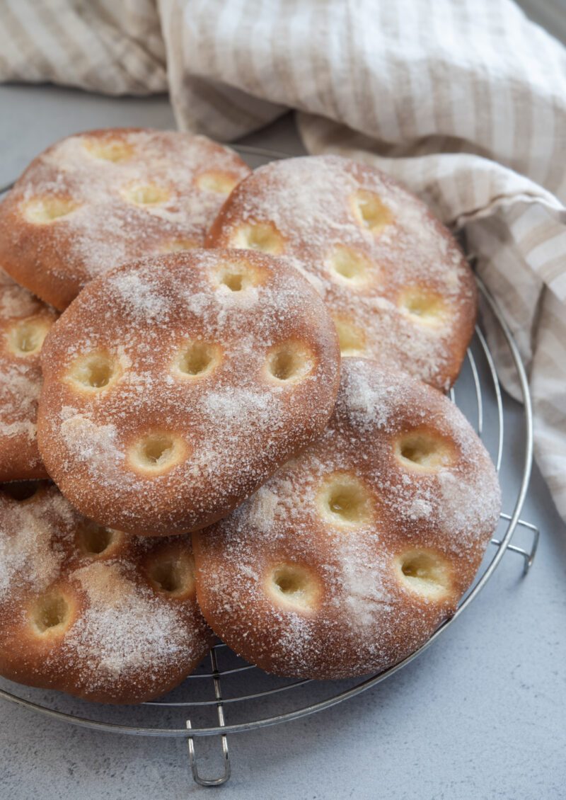 Several flat brioche tart coated with sugar are collected on a round cooling rack.