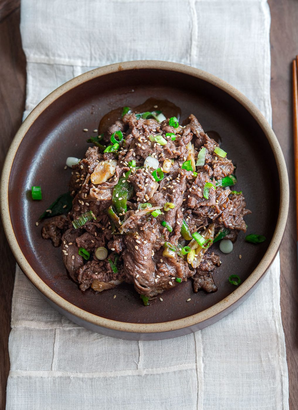 Korean beef bulgogi with glossy caramelized slices and green onion garnish in a brown bowl
