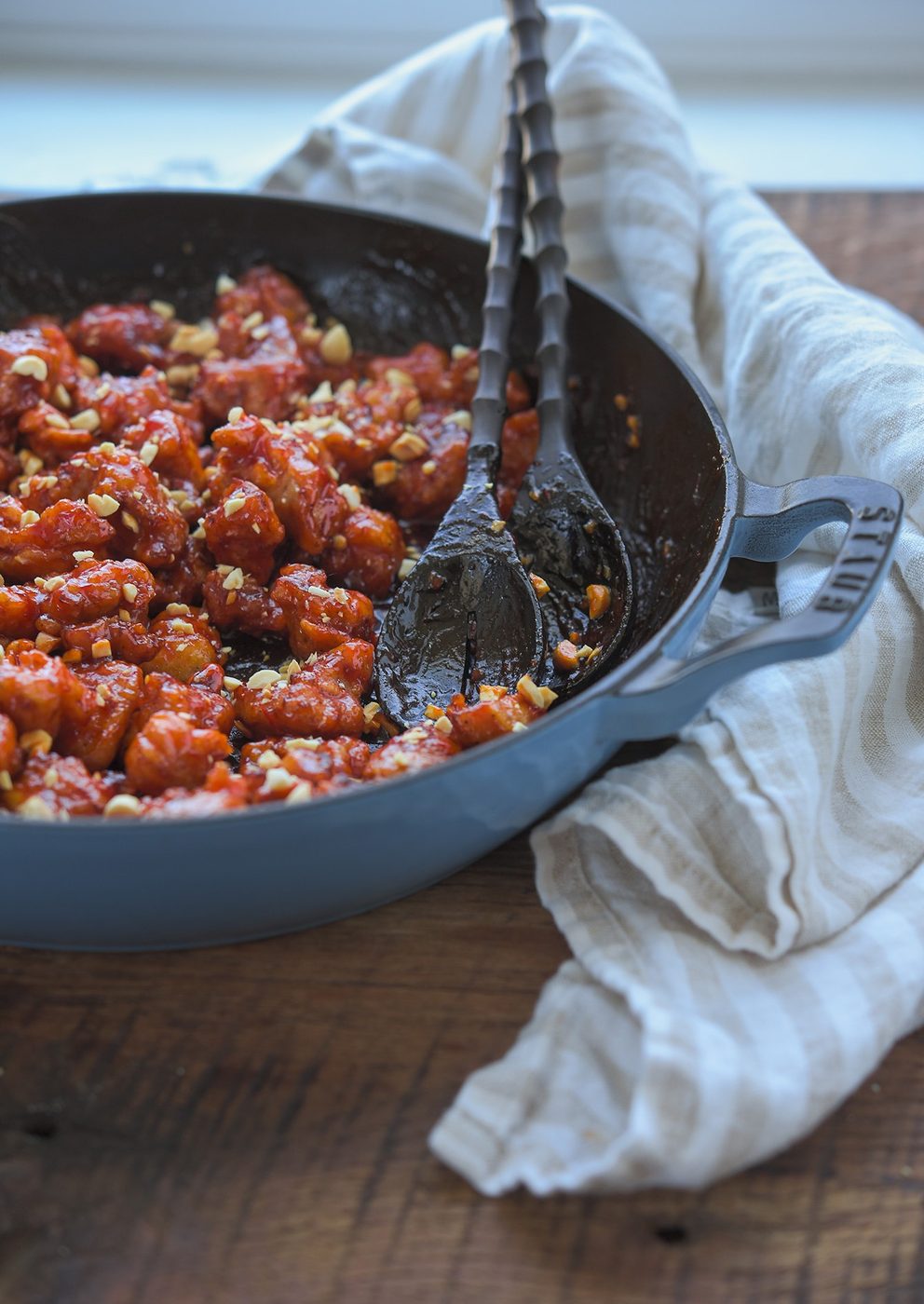 Crispy dakgangjeong coated in glossy glaze in a pan with serving spoons