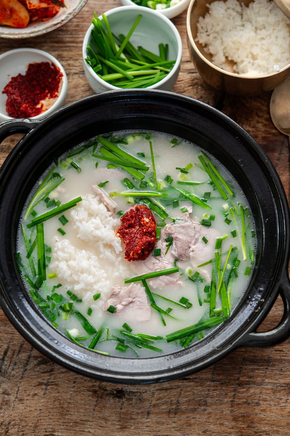 A comforting bowl of Busan-style pork rice soup topped with spicy dadaegi and fresh garlic chives.