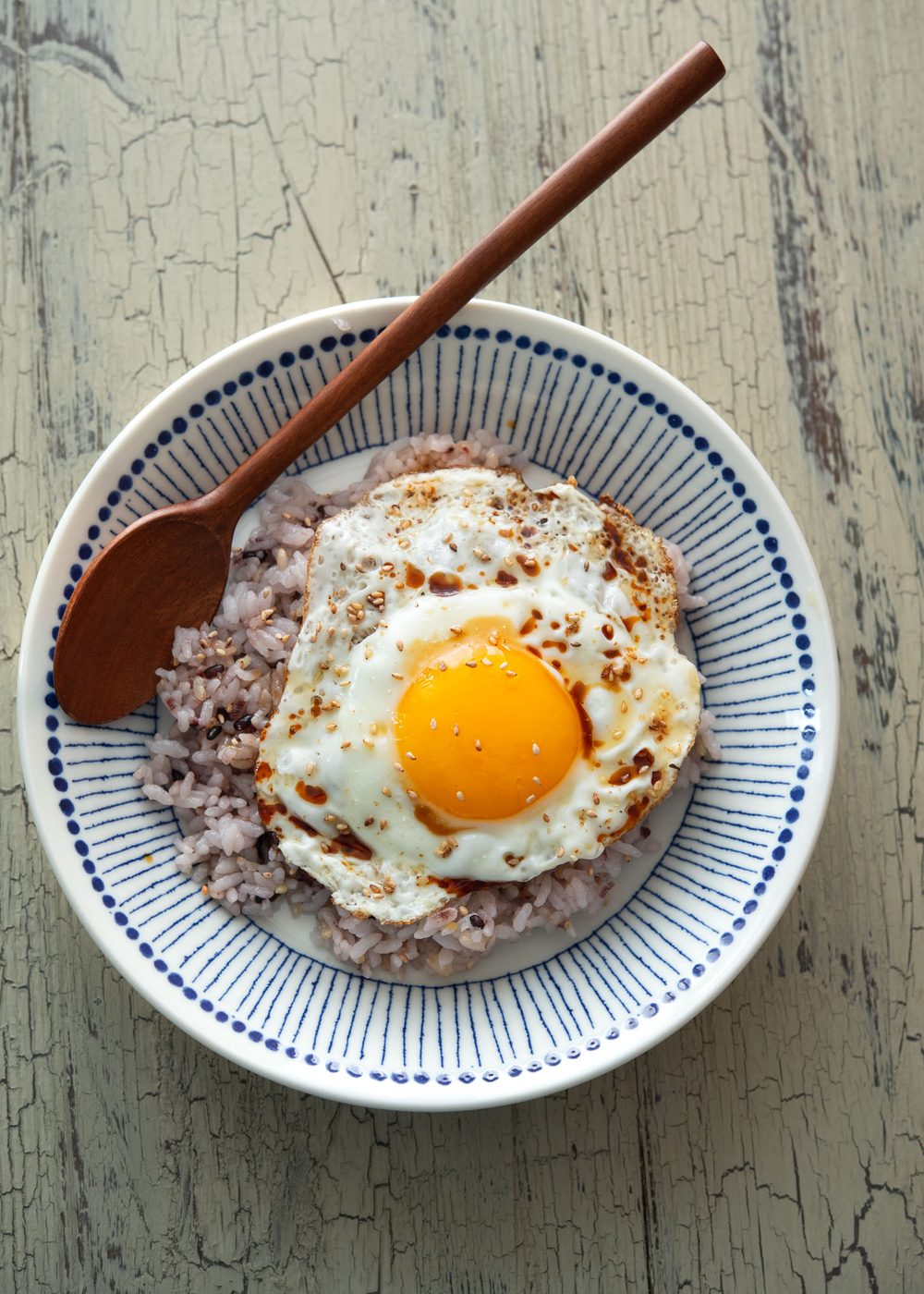 A bowl of gyeran bap is garnished with sesame seeds and served with a spoon.
