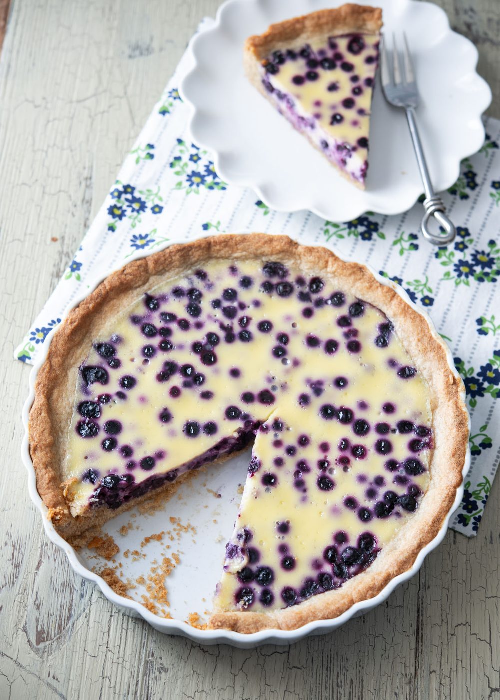 A piece of Finnish blueberry pie is sliced off from a pie dish and served on a small plate.