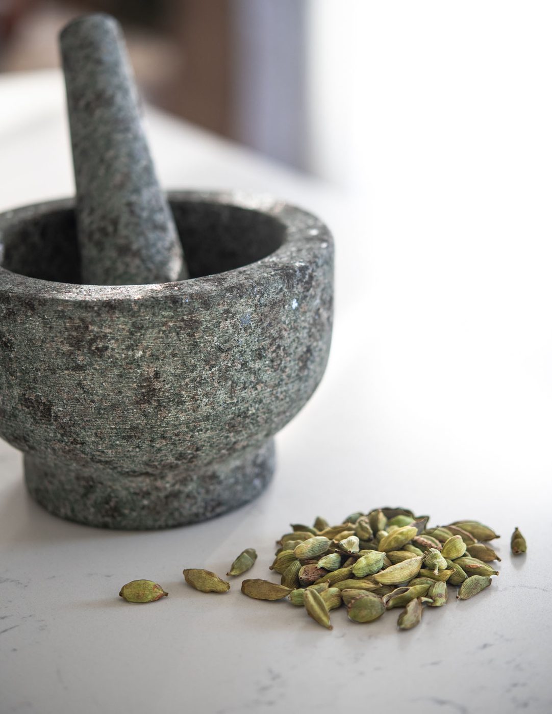 Whole cardamom pods and mortar with pestle for grinding.