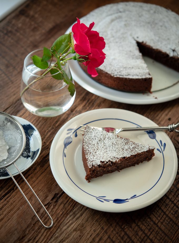 A slice of torta Caprese is garnished with powdered sugar and a rose.