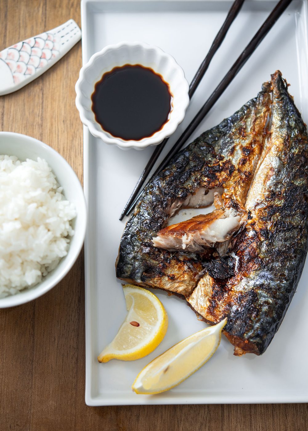 Grilled mackerel is served with soy sauce and lemon wedges in a white plate