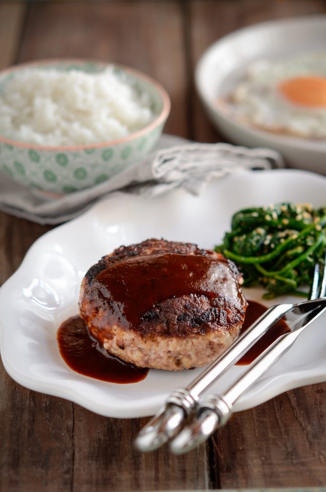 Hambagu is drizzled with red wine sauce and served with rice and spinach.