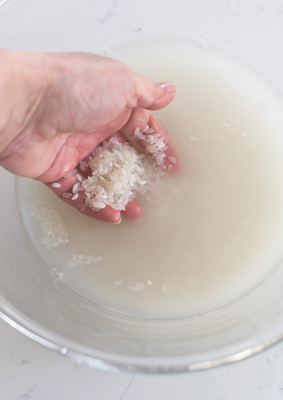 A hand is swirling the rice in water.