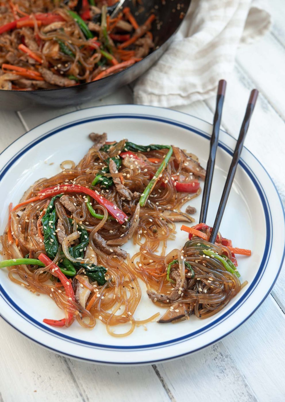 Chopsticks twirled up with japchae noodles on a plate.