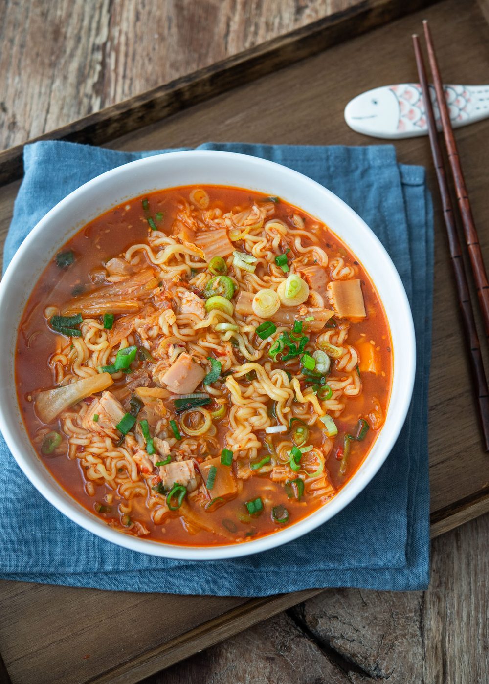 A bowl of kimchi ramen is served on a tray with a pair of chopsticks on the side.