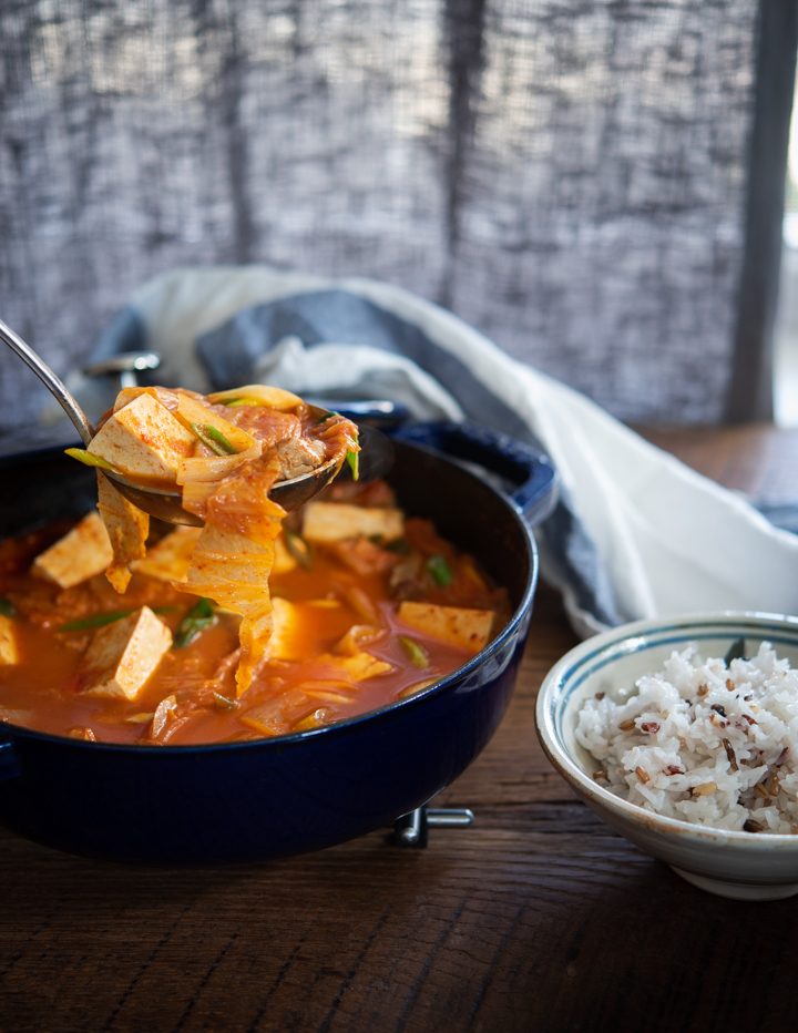 A ladle of kimchi tofu stew served with a bowl of rice.