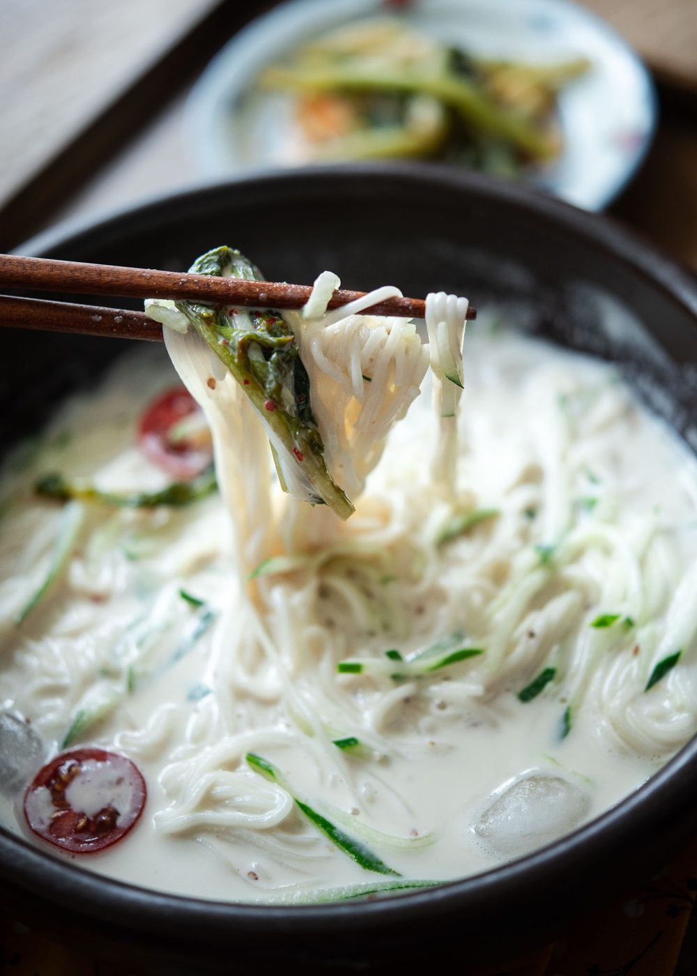 Chopsticks lifting kongguksu noodles from a cold soy milk broth
