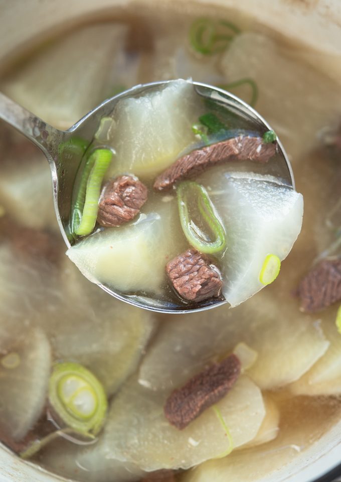 A ladle lifting Korean beef radish soup with clear, translucent broth