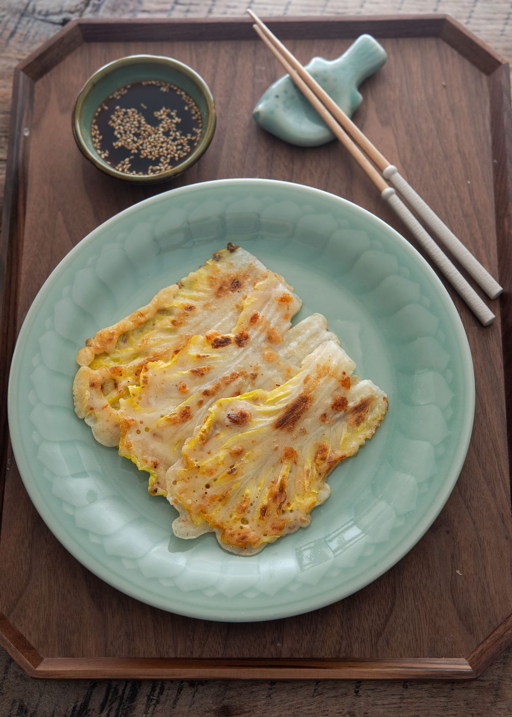 Cabbage pancakes on a plate with dipping sauce and chopsticks.