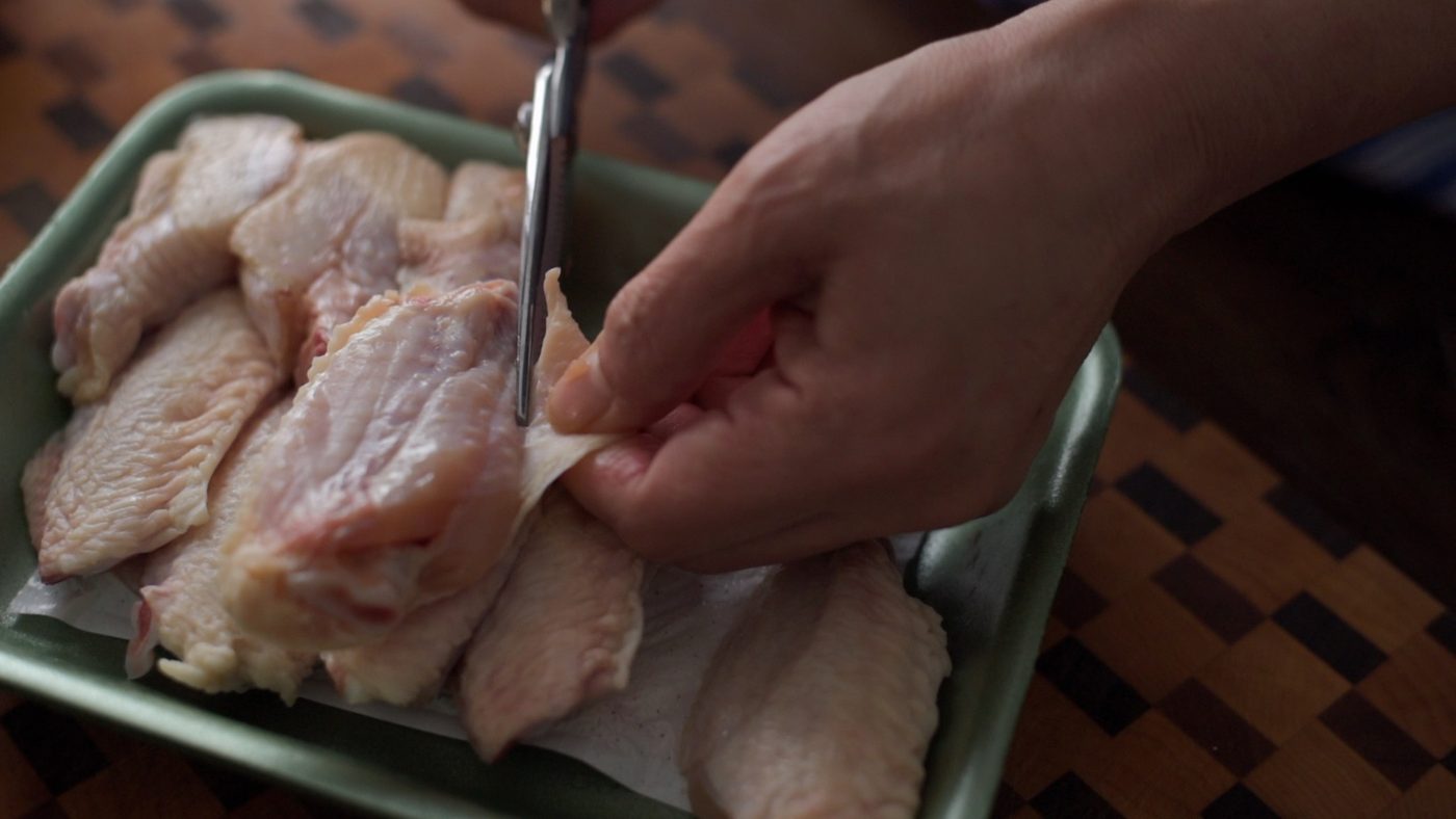 Trimming loose skin from chicken wings with kitchen scissors