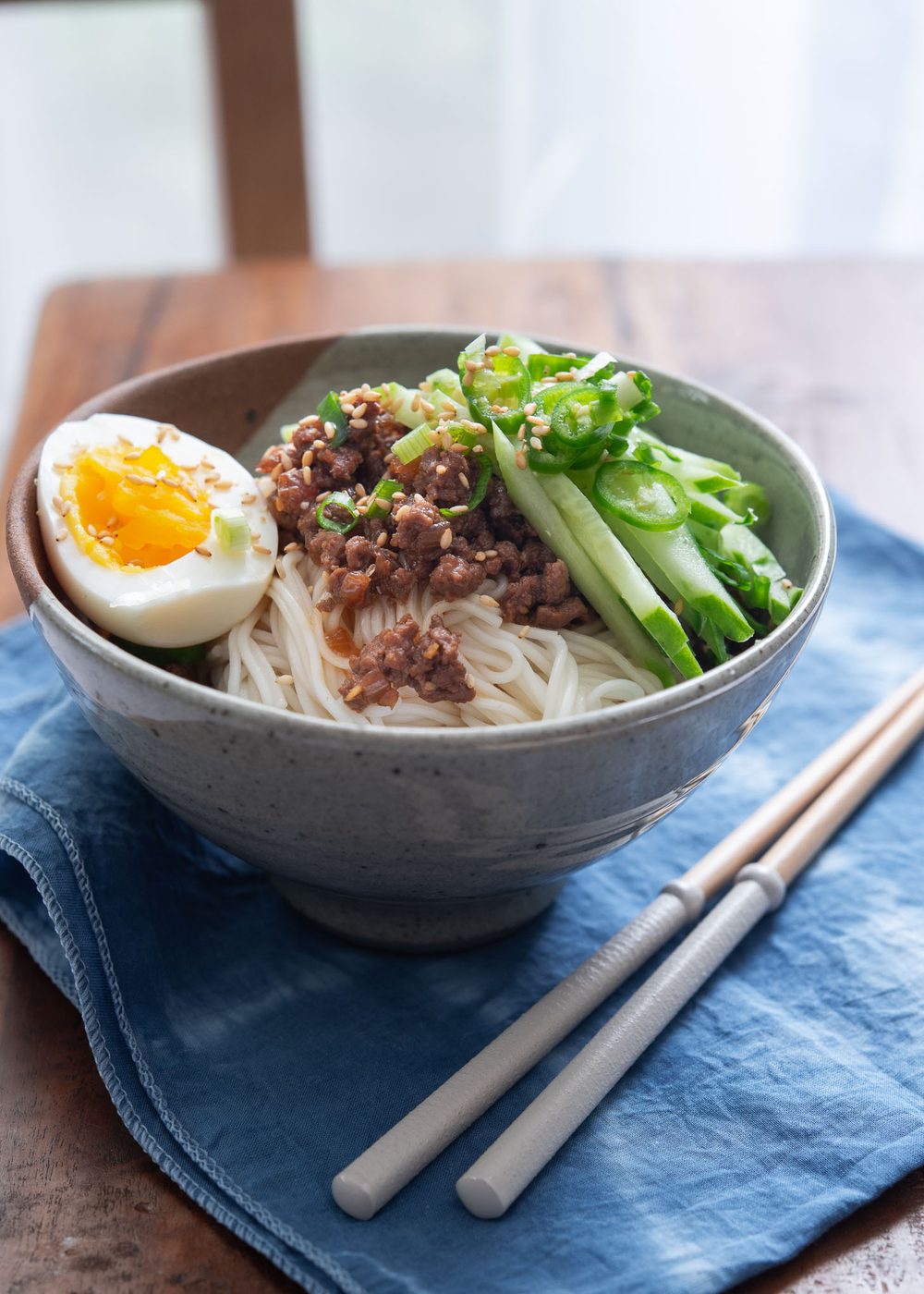 A bowl of noodles with ground beef sauce, cucumber, and hard boiled egg.