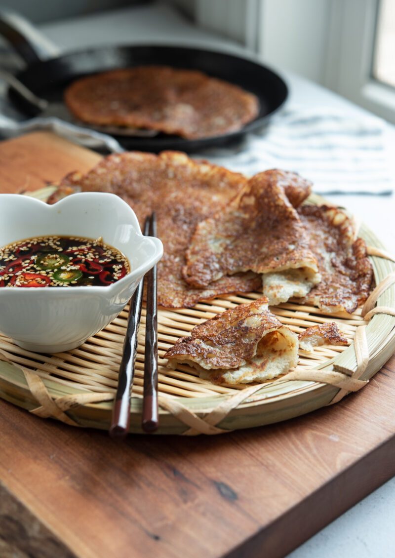 Thin Korean potato pancakes (gamja-jeon) served on a woven plate with soy chili dipping sauce