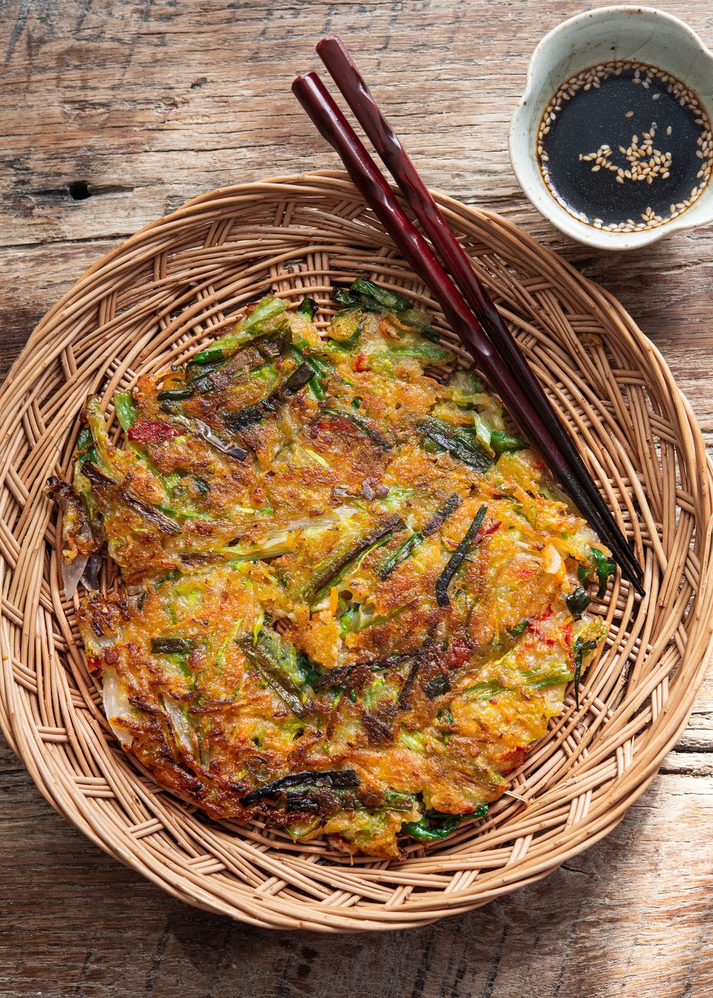 Crispy Korean vegetable pancake (yachaejeon) on a woven basket plate.