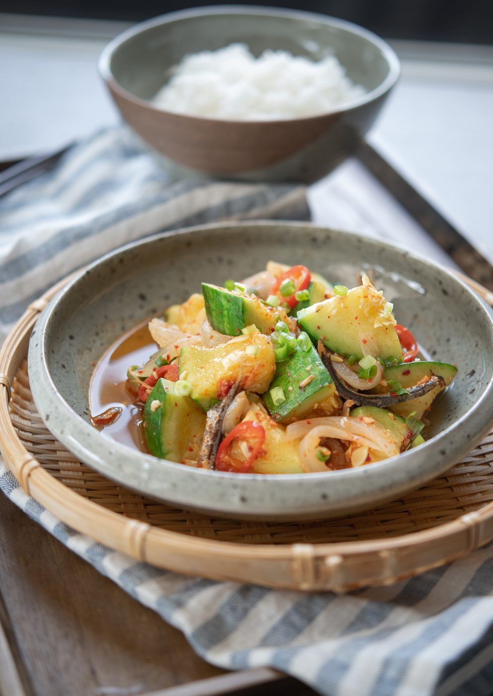Korean round zucchini and anchovy side dish is served in a small bowl on a woven patter