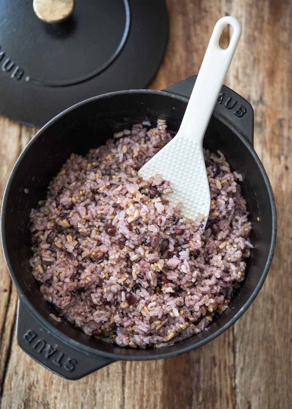Cooked multigrain rice in a pot with a rice paddle, showing purple hue from black rice