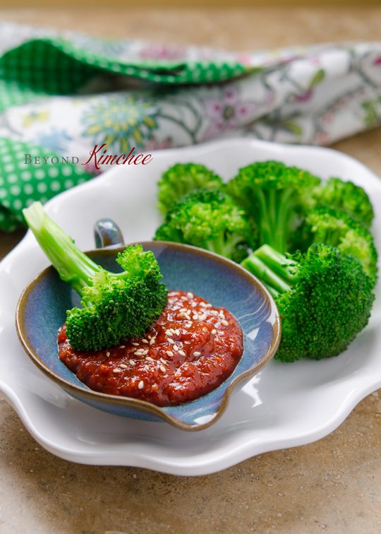 Steamed broccoli florets are served with kitchen-made gochujang sauce in a white serving dish.