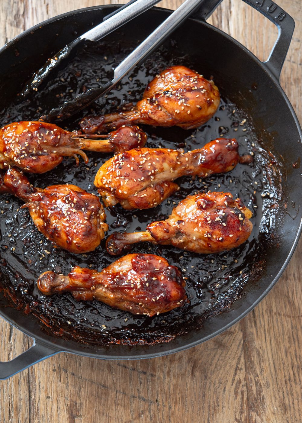Short teriyaki sauce glazed chicken drumsticks in a skillet.