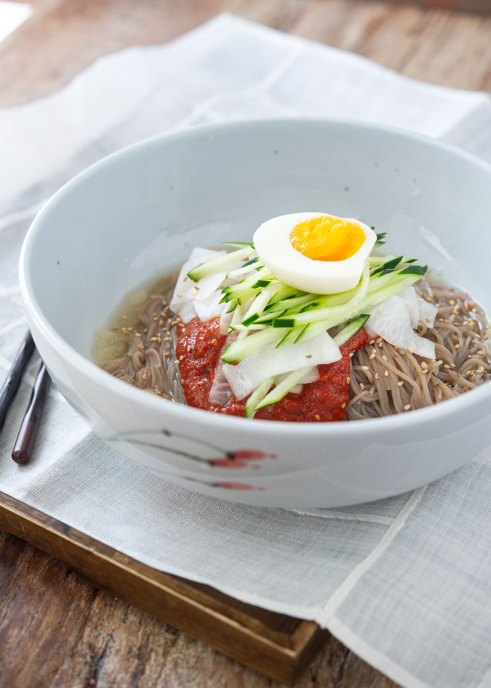 Naengmyeon garnished with bibim naengmyeon sauce and toppings in a bowl.