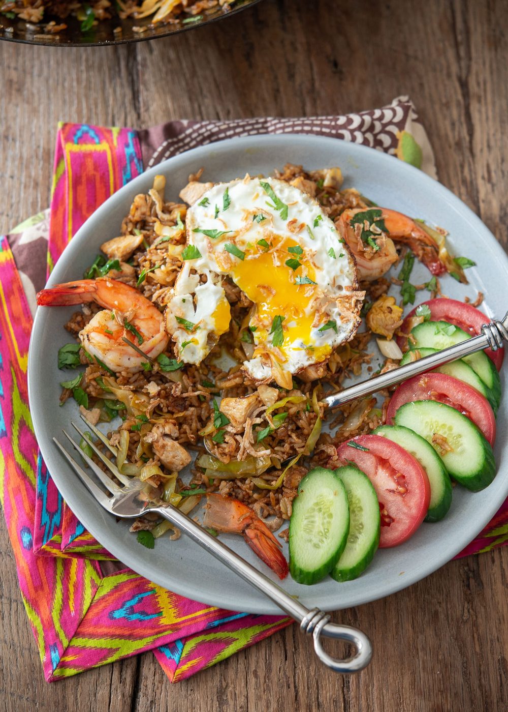 Nasi goreng topped with a fried egg and served with cucumber and tomato.