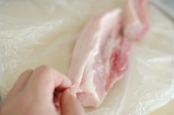 A hand is removing the outer skin of pork belly.