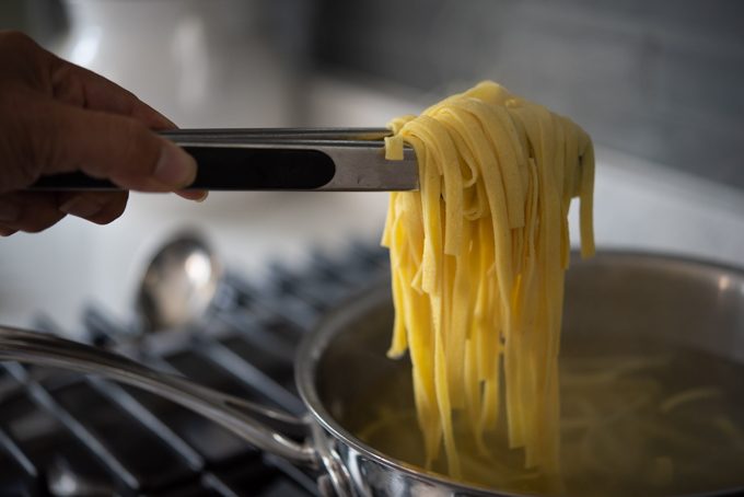 A kitchen tong picking up cooked pasta from a pot.