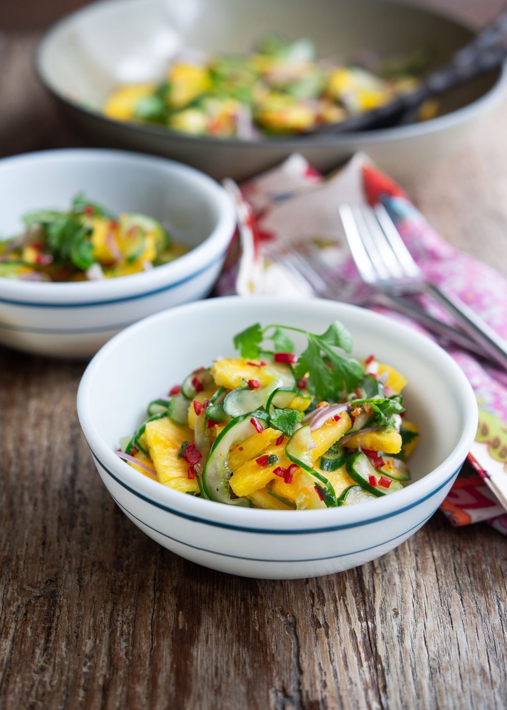 Two small bowls of pineapple cucumber salad garnished with fresh herbs.
