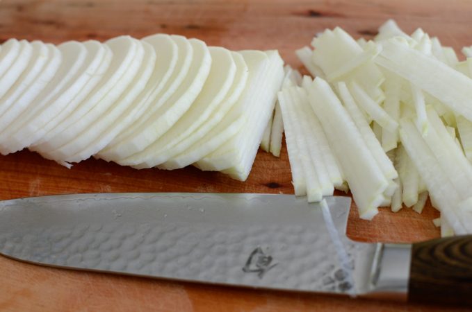 Sliced radish strips and knife on a cutting board.