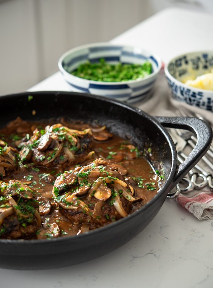 Salisbury Steak with Mushroom Onion Gravy is cooked in a cast iron skillet