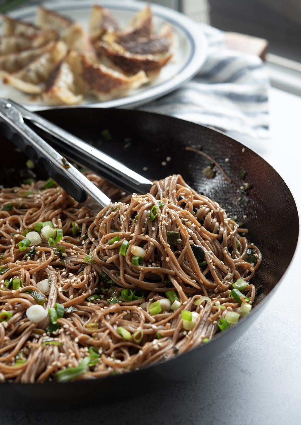 Warm Korean-style sesame soba noodles tossed with green onion in a wok