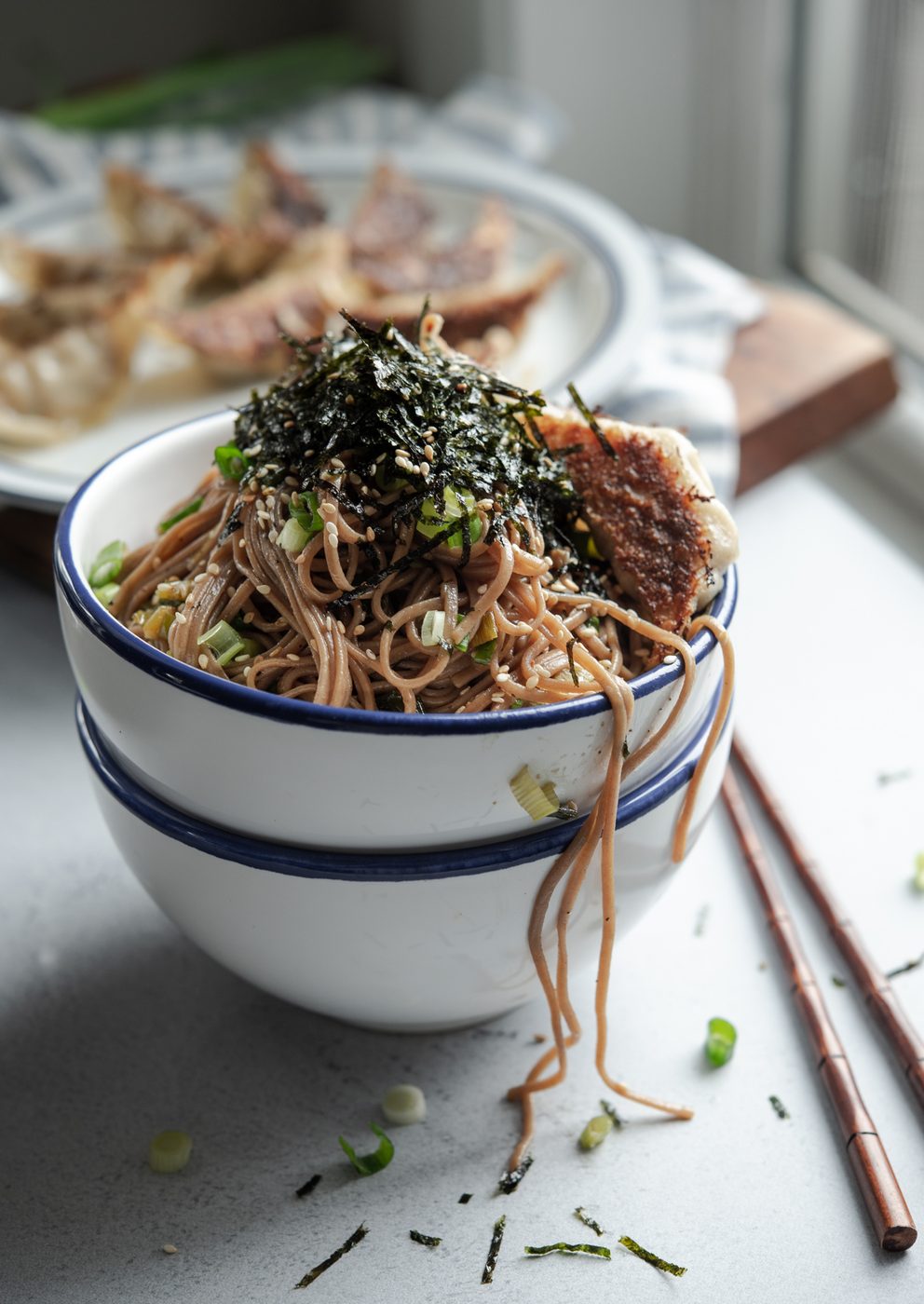Sesame soba noodles are in a bowl topped with crumled seaweed and fried dumplings