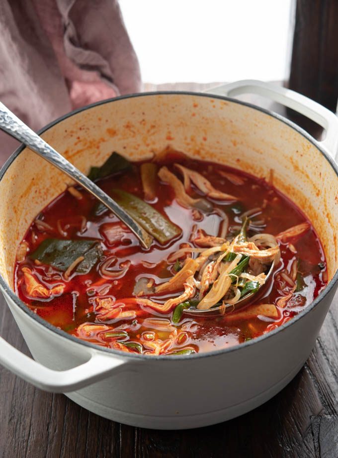 A ladle of dakgaejang, Korean spicy chicken soup with vegetables, resting in a white pot.