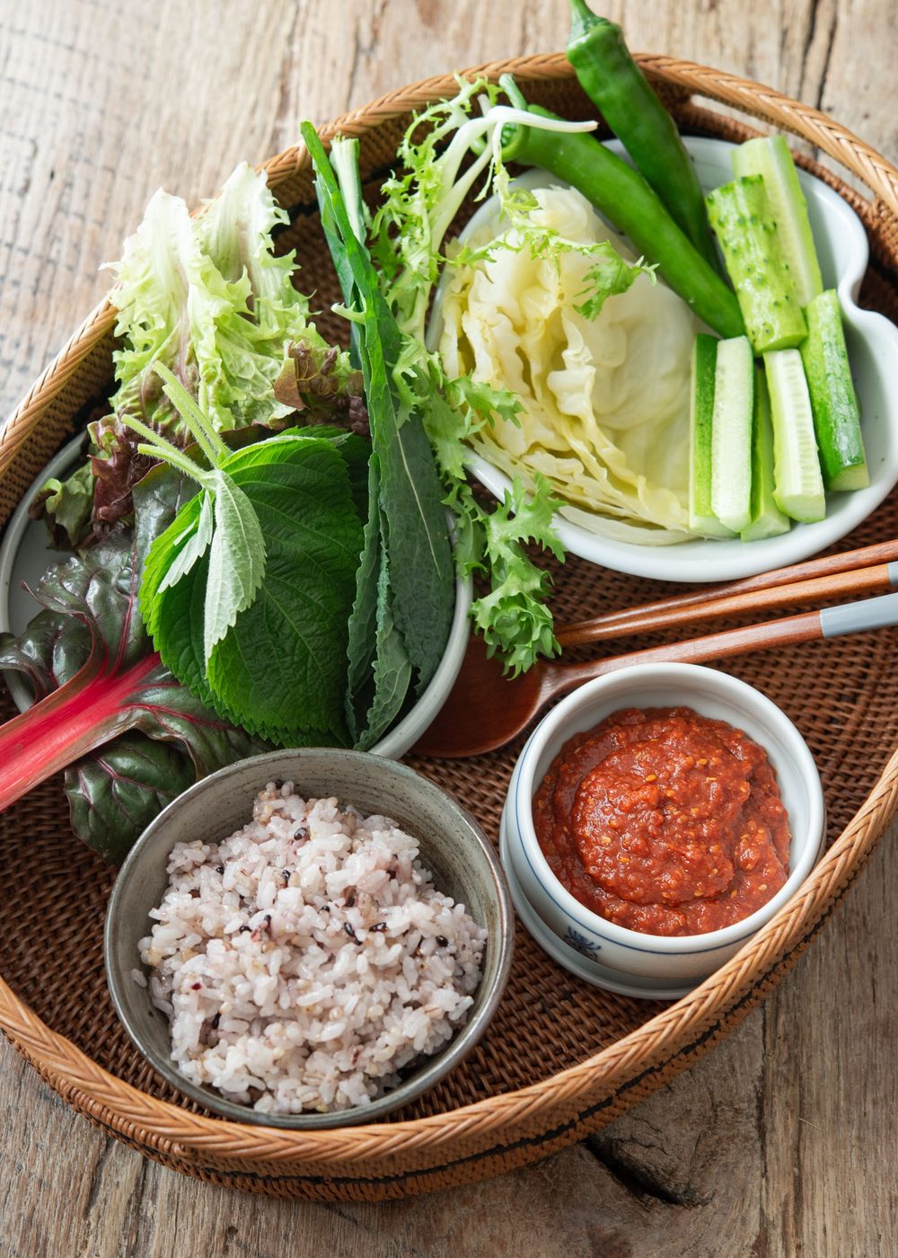 Assorted lettuce and vegetables in a basket with rice and ssamjang sauce