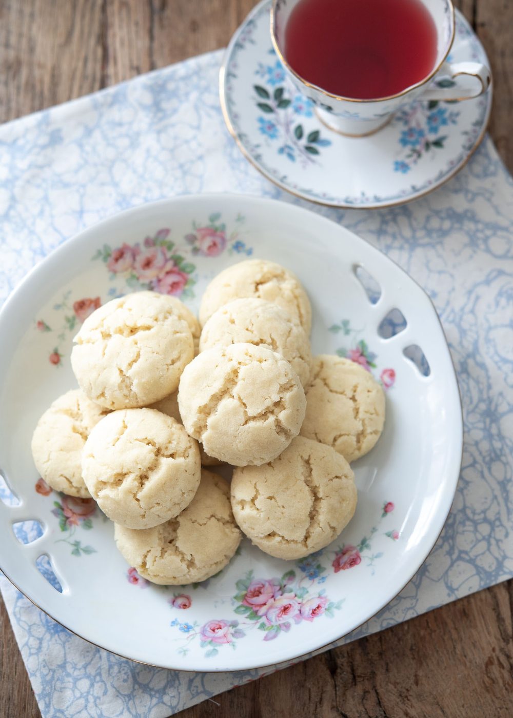A plate of Swedish dream cookies are served with a cup of tea.