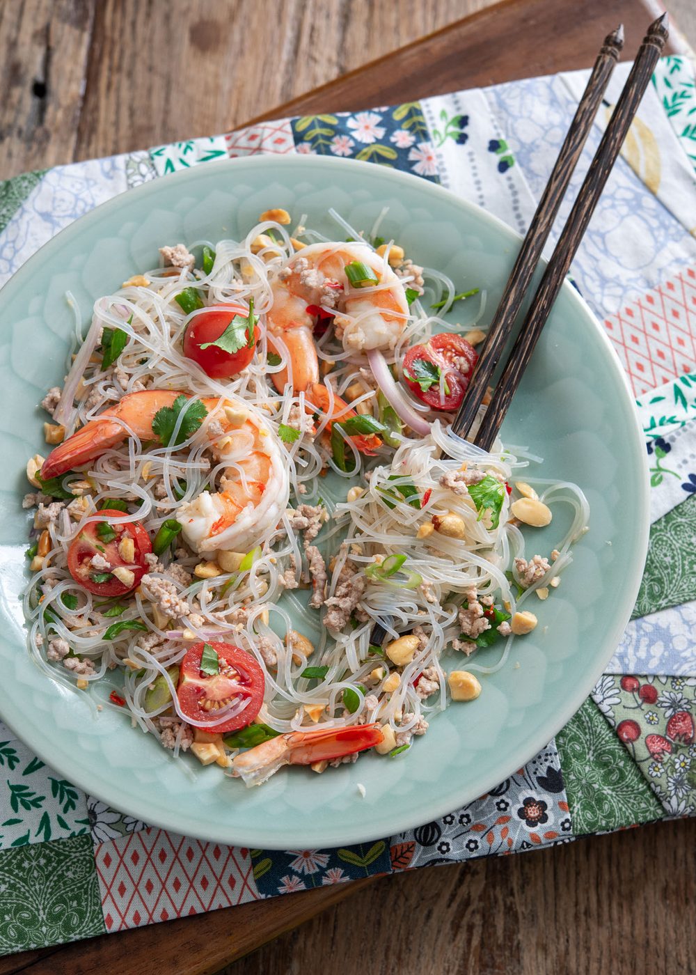 A pair of chopsticks are twirled with glass noodle salad on a green plate.