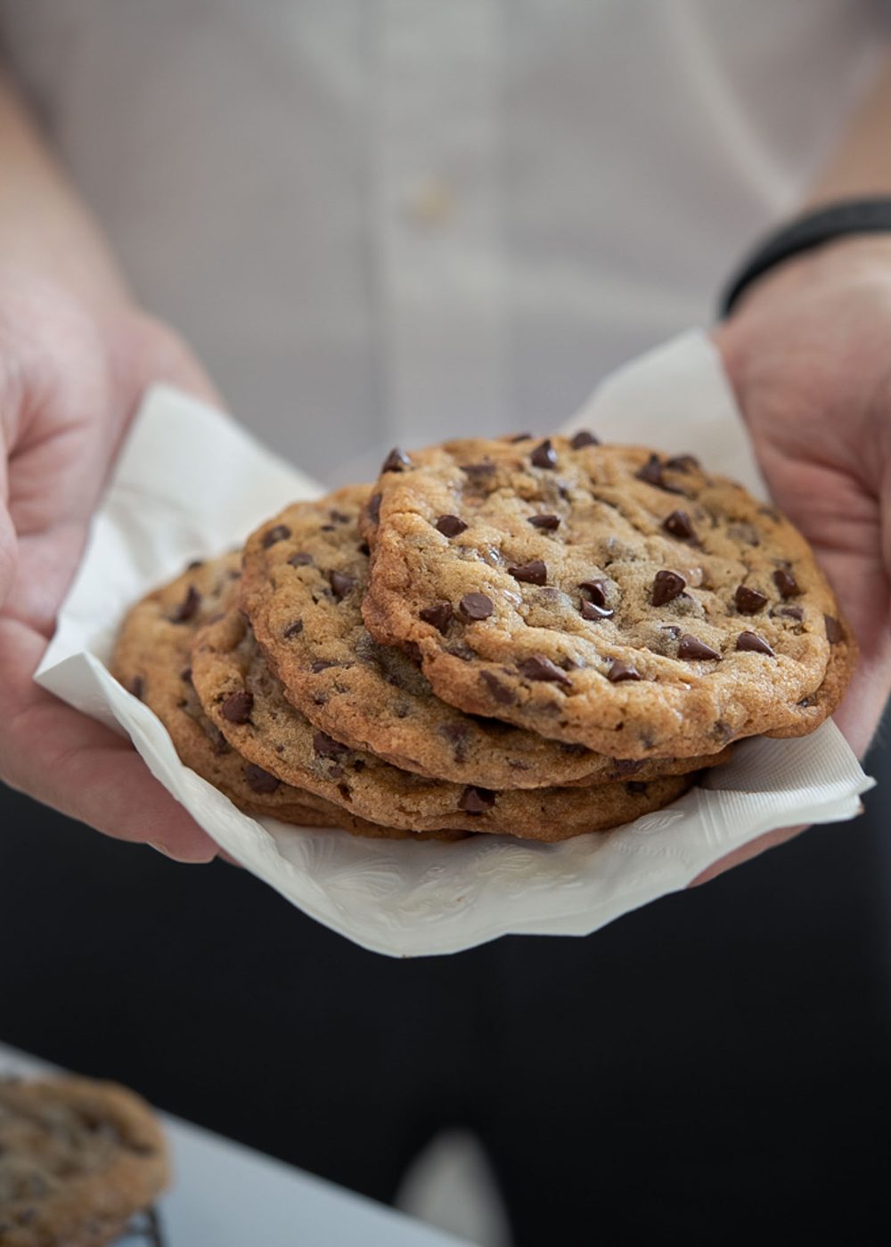 Hands holding stacks of toffee chocolate chip cookies on a napkin.