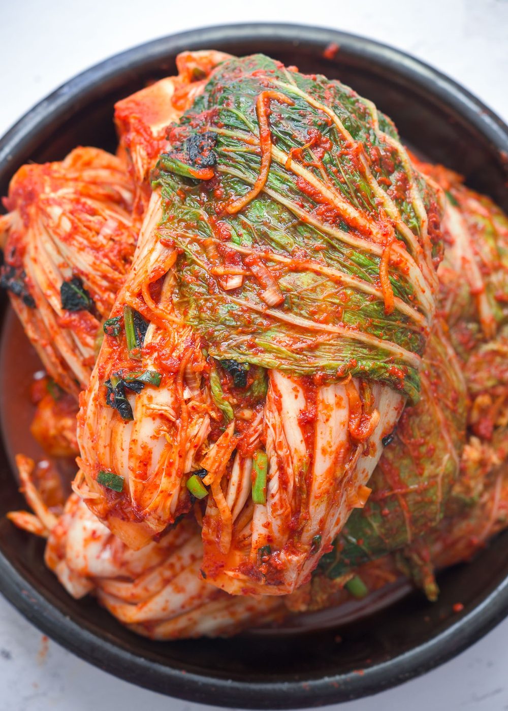 A stack of whole cabbage kimchi bundles in a container.